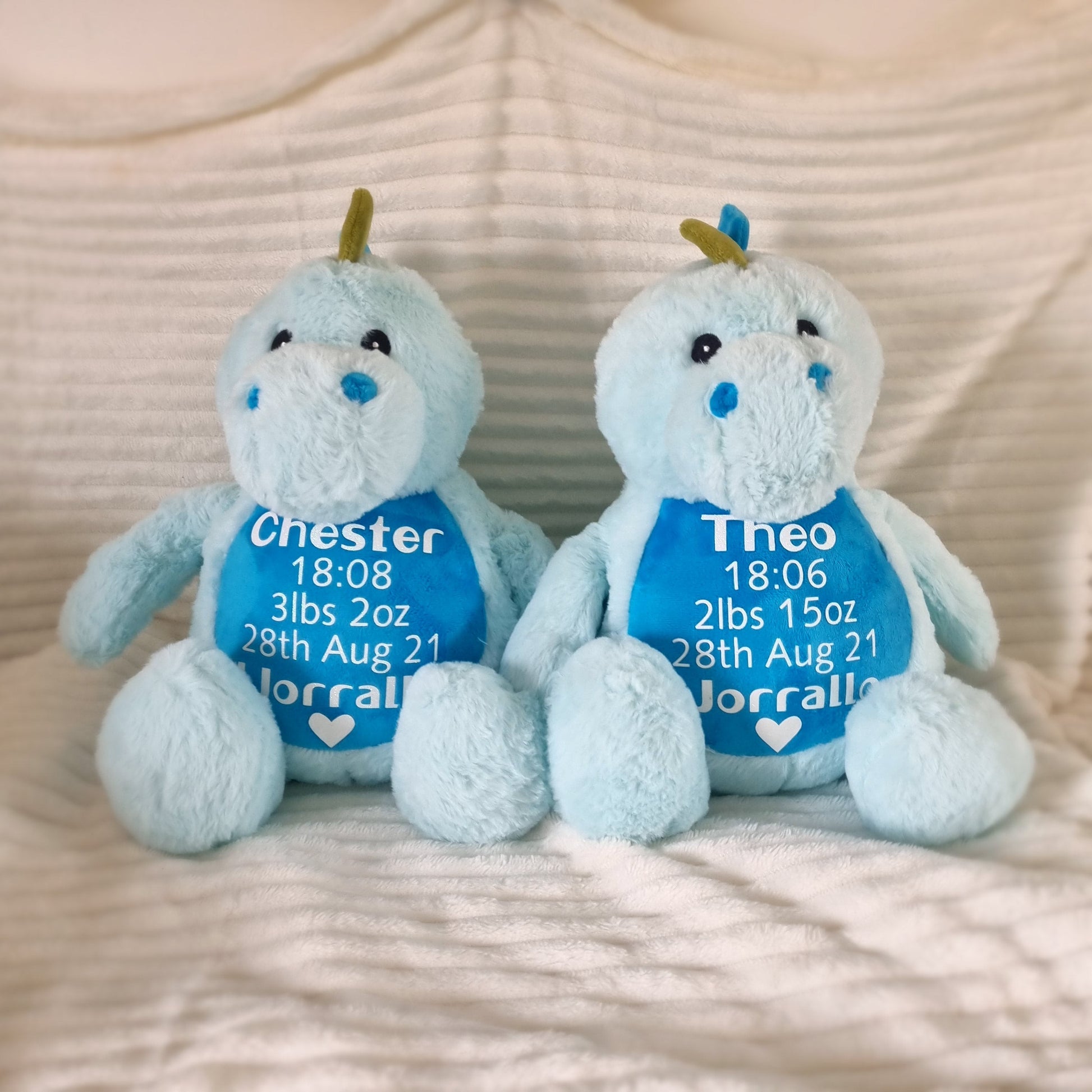 Margot’s birth weight blue dino darlings: two light blue plush toys in personalized bibs